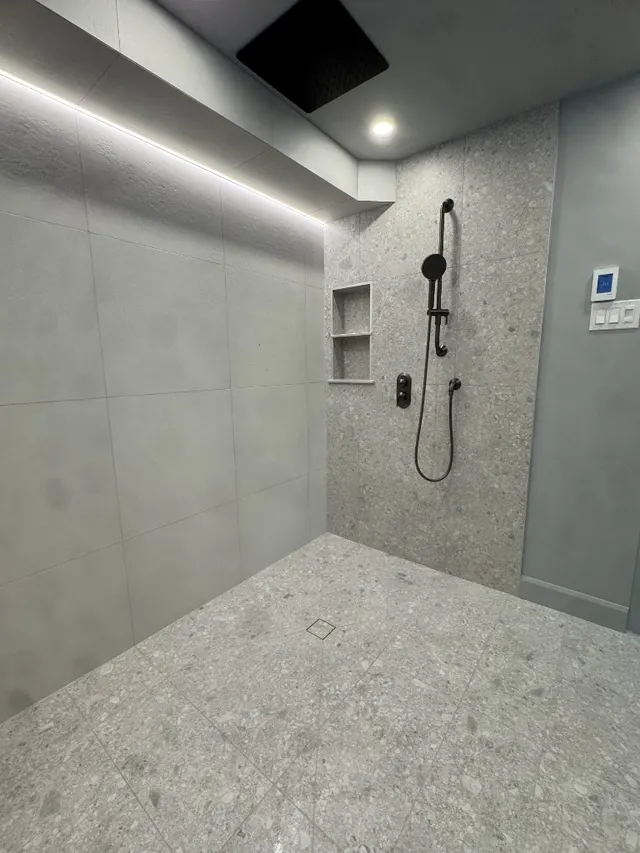 Surface Renaud – terrazzo tile shower with black fixtures and recessed niche